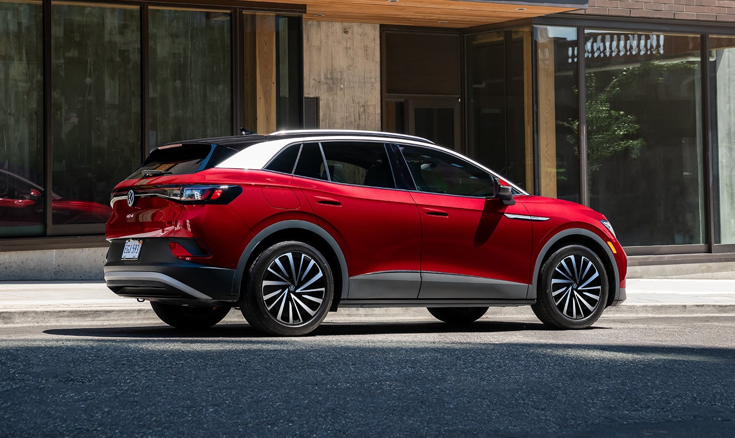An Aurora Red Metallic ID.4 Pro S Plus parked on an urban street in front of a modern building.