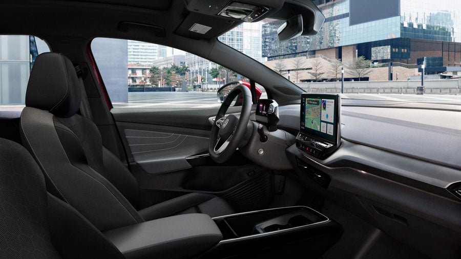 A side view, interior shot of an ID.4 with focus on the driver and passenger seats, steering wheel, dashboard, and center console display with a rock face in the background.